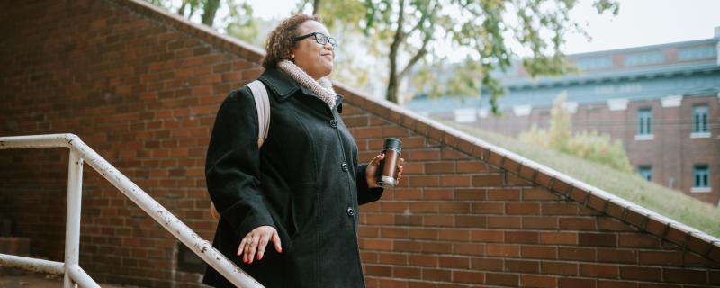 walk in black coat and backpack smiling walking down stairs outside